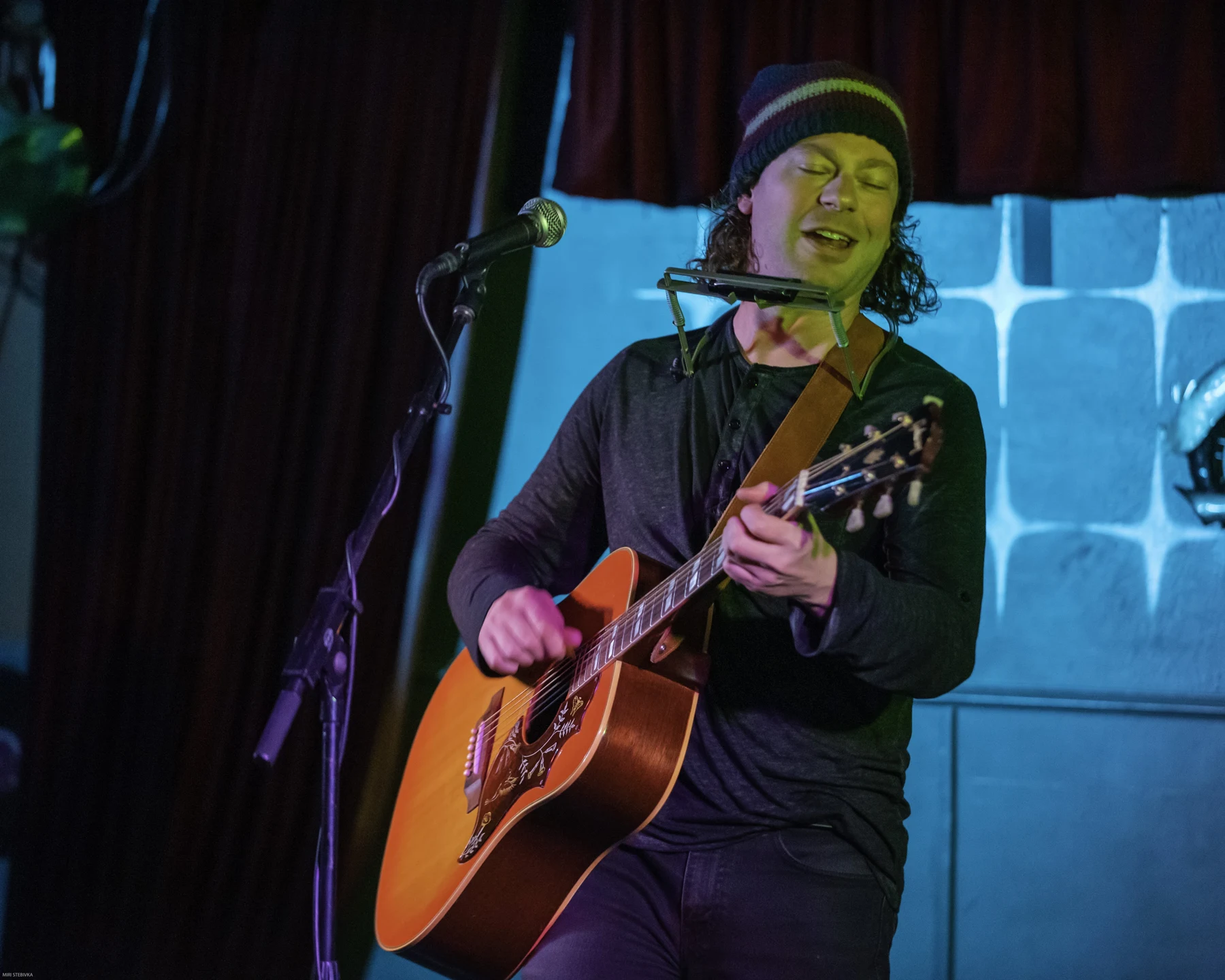 Brian with an acoustic guitar and harmonica onstage